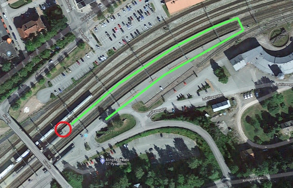 Den framkomliga rutten är märkt på ett flygfoto med grön färg. Rutten går från mellanperrongen via serviceövergången i Helsingfors ändan av bangården till perrongen på järnvägstationssidan.