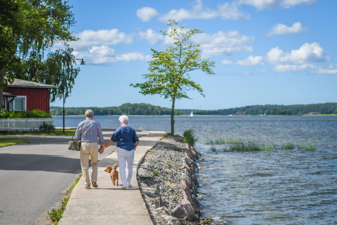 Två äldre personen på promenad med hund vid havet